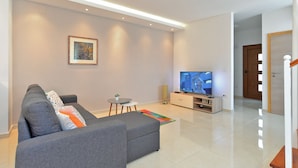Una sala de estar moderna con un sofá gris, una mesita redonda, un televisor y un cuadro en la pared.