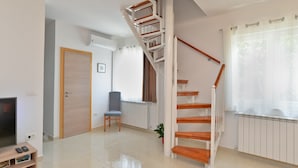 Un salón amplio con una escalera de madera, un radiador, un televisor y una planta en maceta.
