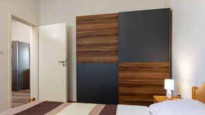 A hotel room with a bed, a nightstand with a lamp, a wardrobe with a wooden panel design, and a door leading to a hallway. - Apartment 1729/17944 (Istria - Pula), 3000m from the beach (Pula)