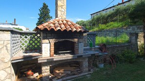 A stone-built outdoor pizza oven with a tiled roof, surrounded by a stone wall and a wooden fence. - Apartment 1729/17944 (Istria - Pula), 3000m from the beach (Pula)