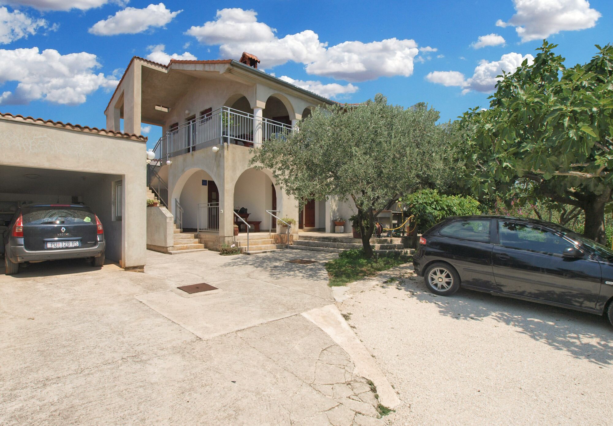Une maison à deux étages avec un balcon, un garage et un arbre dans la cour.
