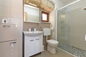 A bathroom with a white sink, toilet, and shower. There is a mirror above the sink and a window above the toilet.
