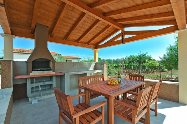 An outdoor patio with a wooden table and chairs, a barbecue grill, and a view of a vineyard. - House 1735/17984 (Istria - Galižana), 5000m from the beach (Galižana)