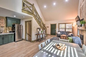 A spacious loft with a high ceiling, a staircase, a kitchen with modern appliances, a dining area with a table set for four, and a cozy seating area with a sofa and a fireplace.