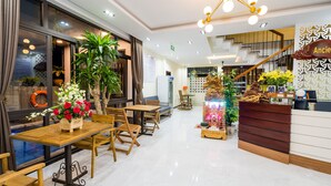 A hotel lobby with wooden tables and chairs, a reception desk, and a staircase.
