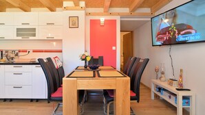 A modern kitchen with white cabinets, a wooden dining table with black chairs, and a TV mounted on the wall displaying a news channel. - Apartment 1739/17997 (Istria - Medulin), 50m from the beach (Medulin)