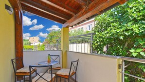 A covered outdoor seating area with a table and four chairs, a bottle on the table, and a view of a garden and buildings in the background. - Apartment 1739/17997 (Istria - Medulin), 50m from the beach (Medulin)