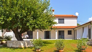 Une maison à deux étages, avec un toit en tuiles, un mur en pierre et des plantes en pot dans le jardin.