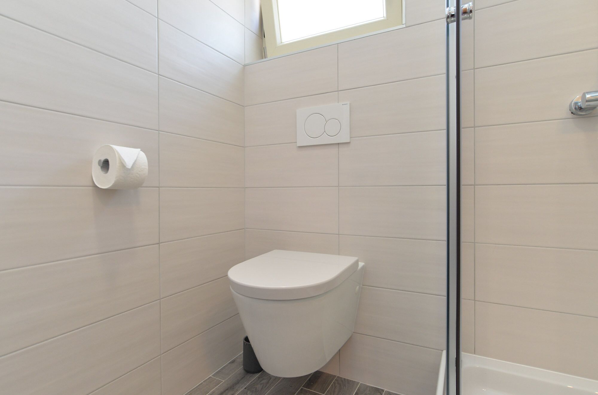 A small, modern bathroom with a toilet, a shower, and a toilet paper holder.