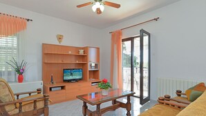 A living room with a television, wooden furniture, a glass coffee table, and a view through a sliding glass door. - Apartment 1755/18834 (Istria - Svetvinčenat), 20000m from the beach (Svetvincenat)