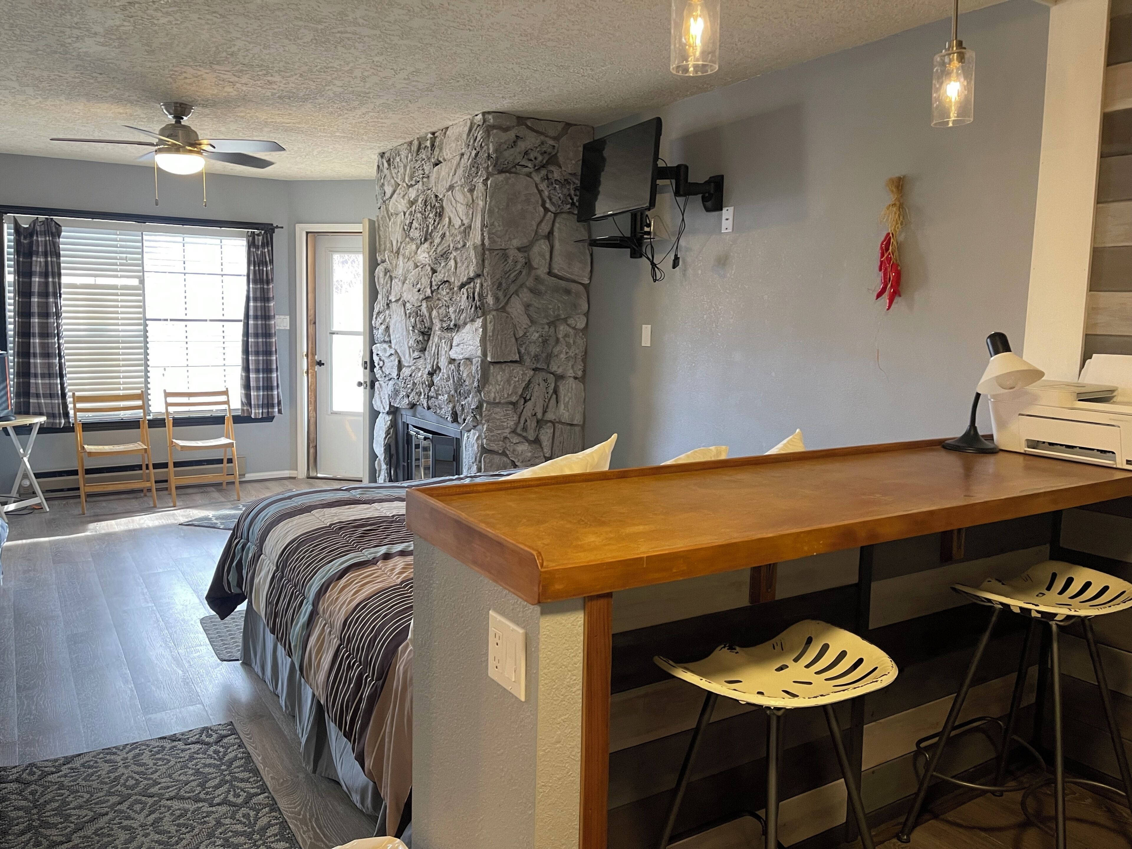 Una sala moderna con una pared de acento de piedra, una mesa de comedor de madera con taburetes de bar, un ventilador de techo y una chimenea.