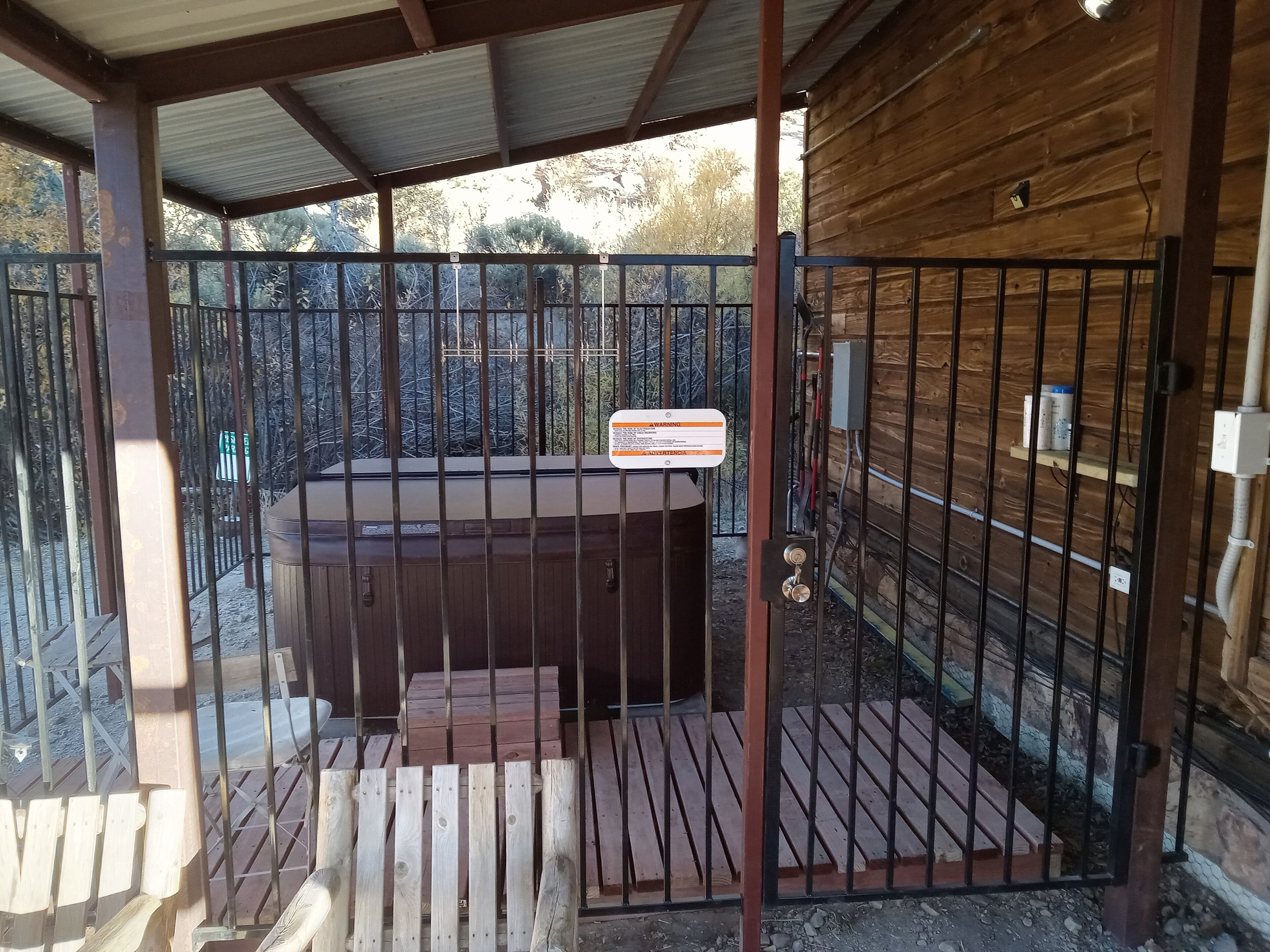 Una cabaña de madera con hidromasaje, portón metálico y un cartel de advertencia.