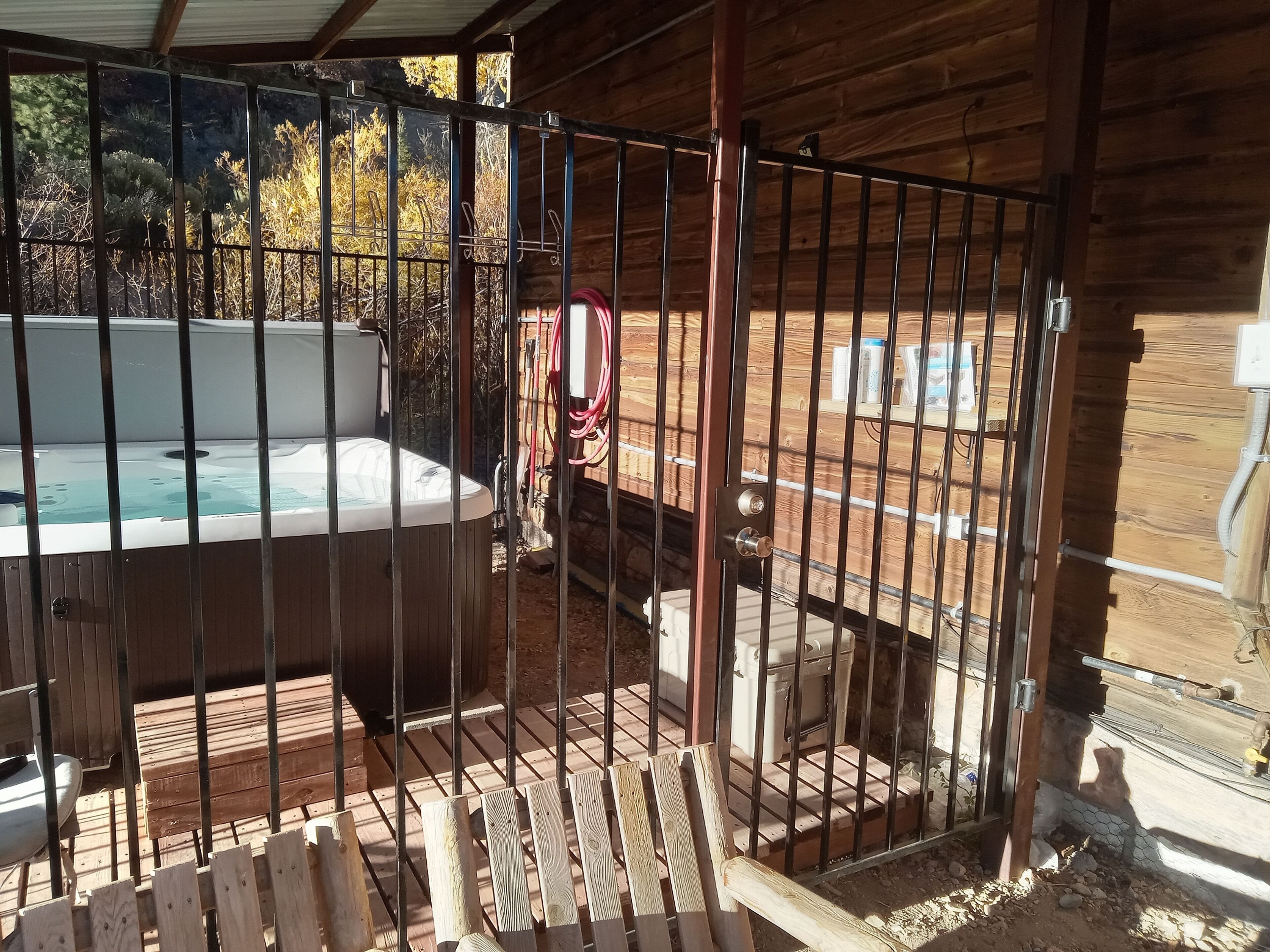 Un bain à remous entouré d’une clôture en métal, avec une terrasse en bois et un mur de briques en arrière-plan.