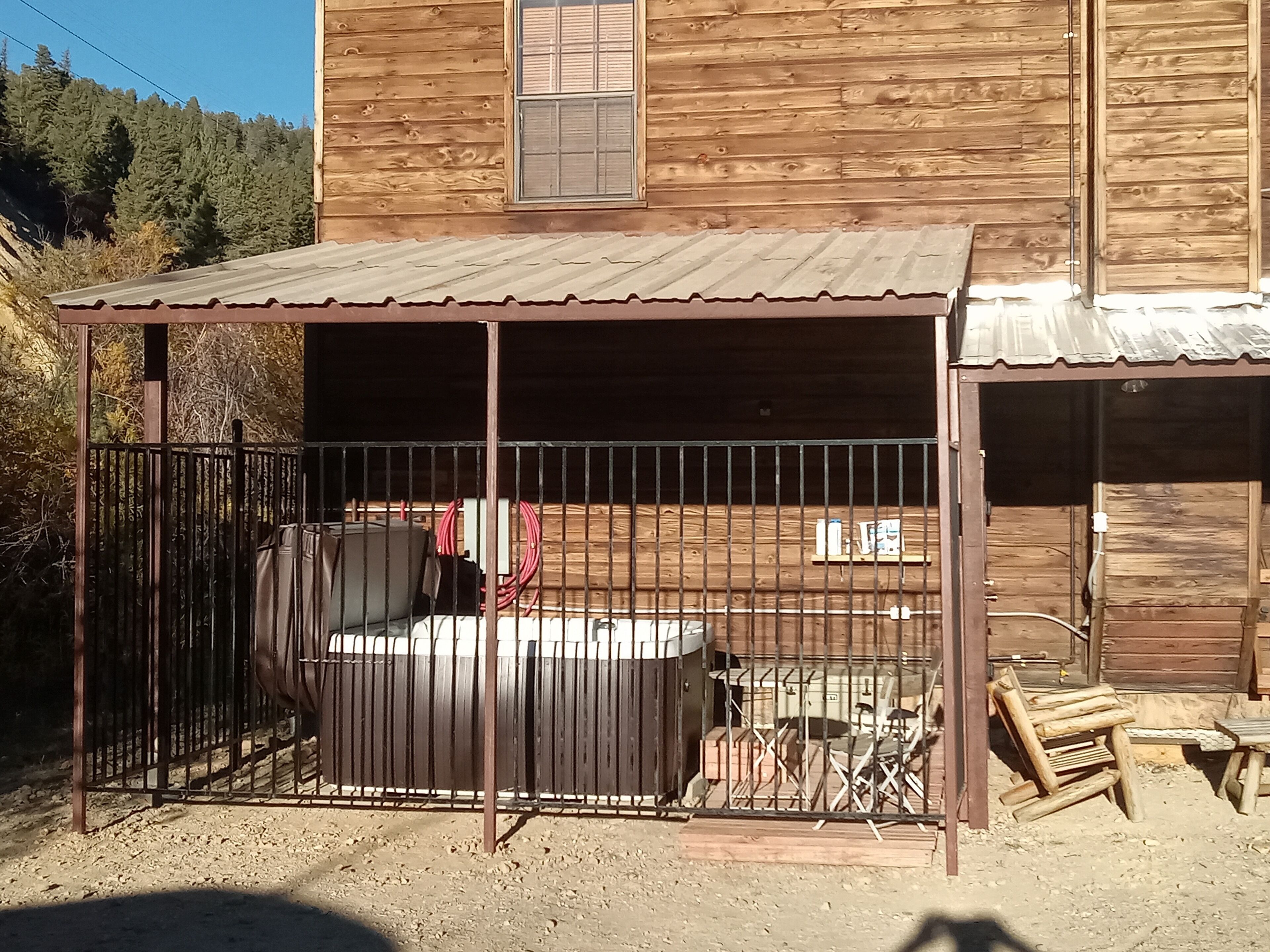 A rustic wooden building with a covered patio area, a fenced enclosure, and a small wooden structure.
