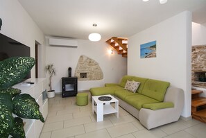 A living room with a green sofa, a small white table, a stone fireplace, and a television. - House 1765/19674 (Istria - Peroj), 1000m from the beach (Peroj)