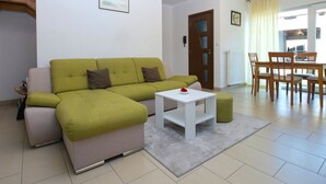 A living room with a green sofa, a white coffee table, and a dining area with wooden chairs and a table. - House 1765/19674 (Istria - Peroj), 1000m from the beach (Peroj)