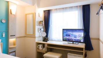 Une chambre d’hôtel comprenant un lit, un bureau avec un écran d’ordinateur affichant un horaire de train, un téléphone et un petit placard.