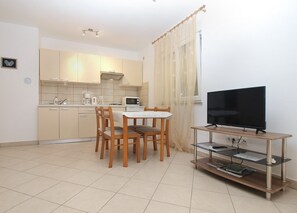 Een functionele woonruimte met een kitchenette, een eethoek met tafel en stoelen, en een televisie op een standaard.