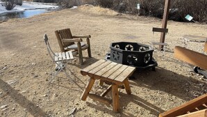 A rustic outdoor seating area with a wooden table and chairs, a fire pit, and a view of a river and mountains. - Riverbend 8A Townhouse (Red River)