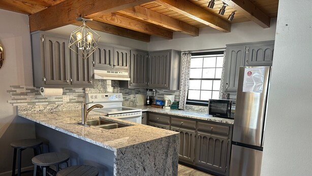 A kitchen with granite countertops, stainless steel appliances, and wooden bar stools. - Riverbend 8A Townhouse (Red River)