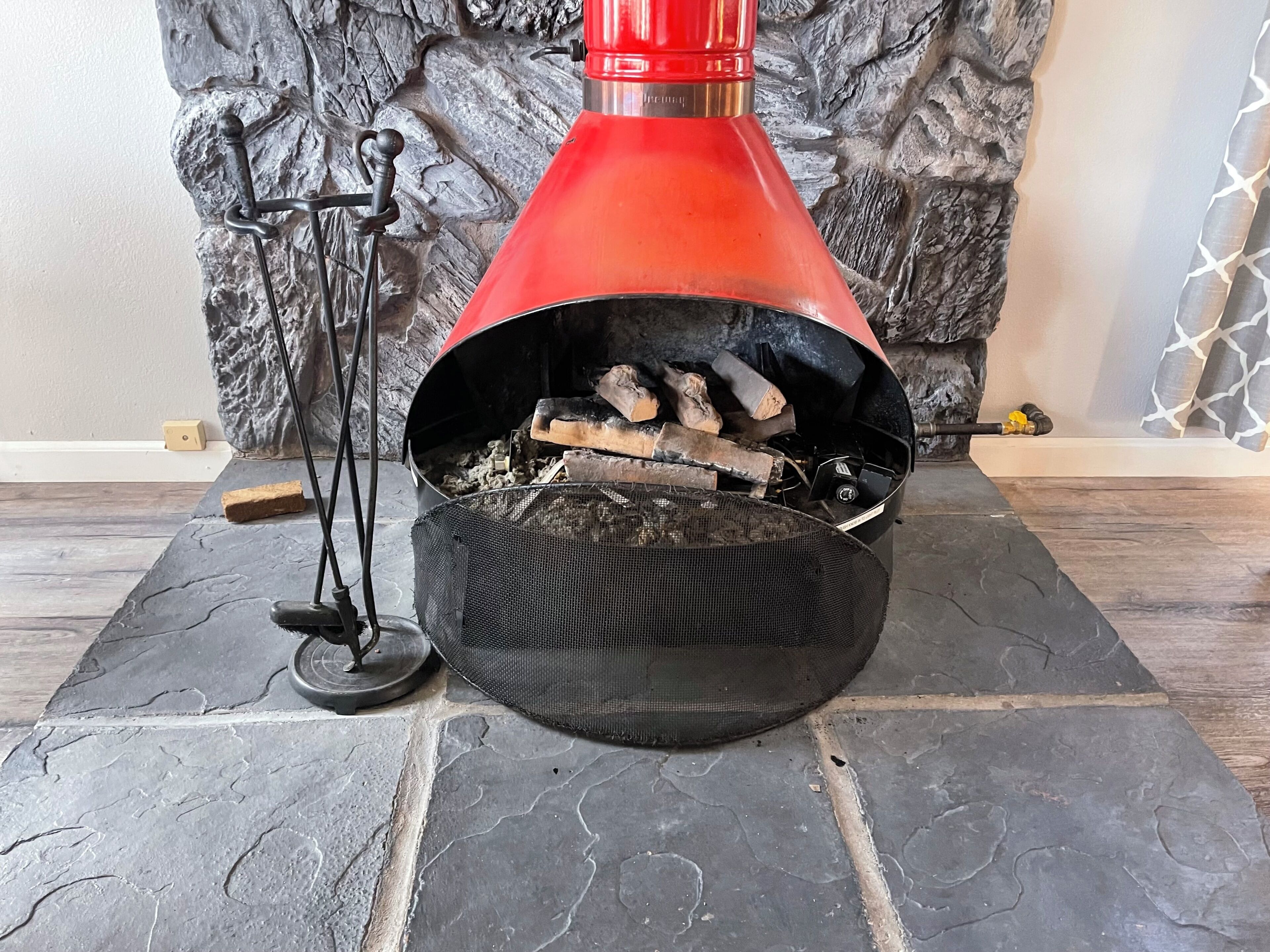 A fireplace with a red chimney, a mesh screen, and logs inside.