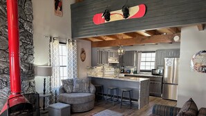 A cozy living area with a fireplace, a sofa, a patterned rug, and a kitchen with a bar. - Riverbend 8A Townhouse (Red River)