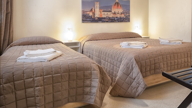 Quarto de hotel com duas camas, cada uma com colcha acolchoada marrom e toalhas dobradas com cuidado.