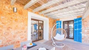 A dining area with a stone wall, a wicker chair, and a table set for two. - Bona Vista with private pool, A/C, table tennis, WiFi, quiet location (Felanitx)