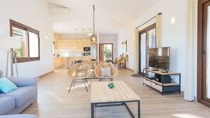 A modern living room with a sofa, a coffee table, wicker chairs, a TV, and a kitchen in the background. - Bona Vista with private pool, A/C, table tennis, WiFi, quiet location (Felanitx)