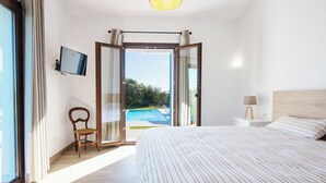 A hotel room with a bed, a TV, a chair, a nightstand, and a view of a swimming pool. - Bona Vista with private pool, A/C, table tennis, WiFi, quiet location (Felanitx)