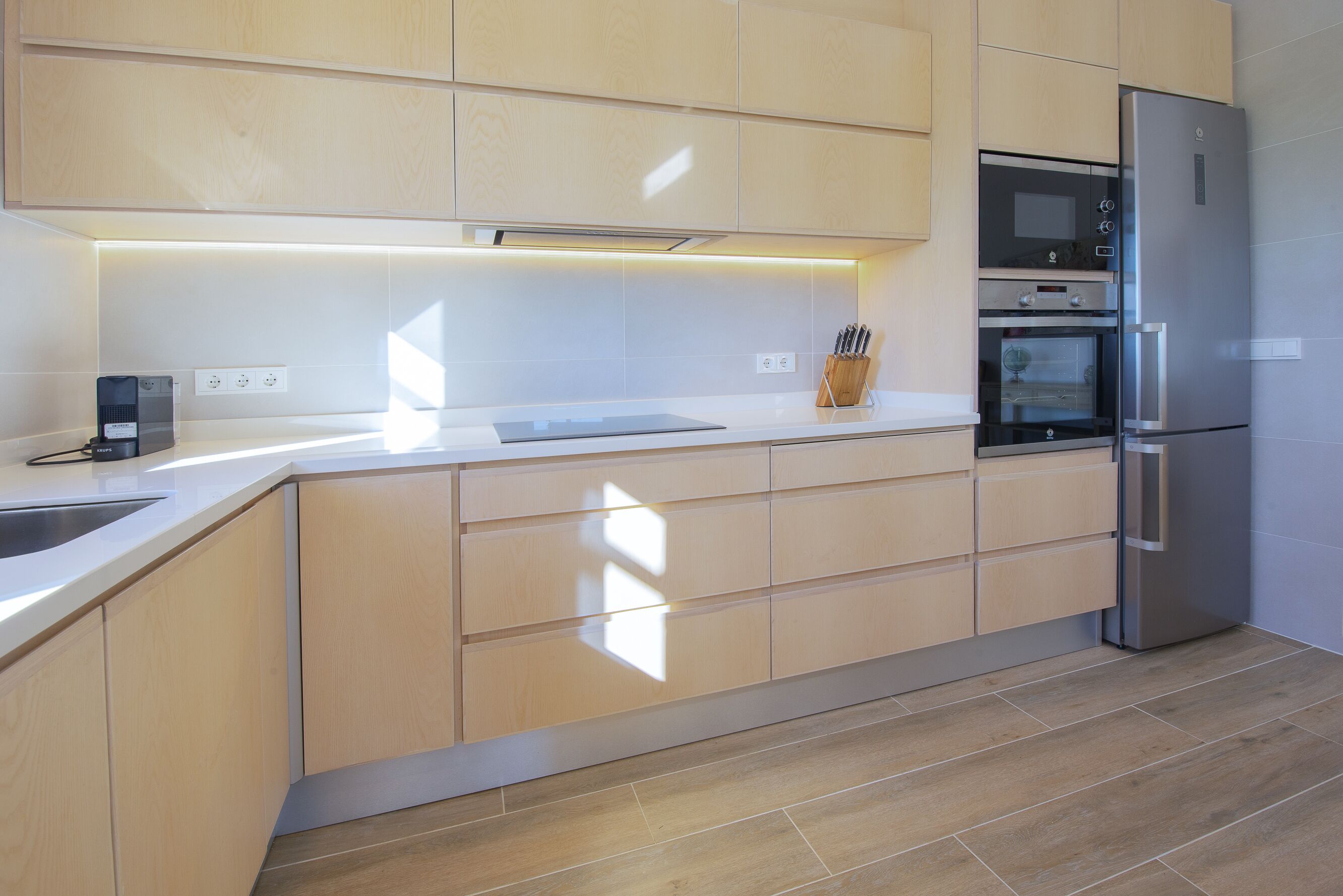 Una cocina moderna con armarios de madera clara, un refrigerador de acero inoxidable, un horno empotrado y una encimera con una cafetera.