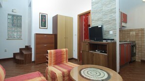 A compact living space with a sofa, a small round table, a television on a wooden cabinet, and a kitchen area with a stove and cabinets. - Apartment 1775/20467 (Istria - Medulin), 750m from the beach (Medulin)