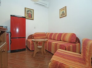 A compact living space with a red refrigerator, a striped sofa, a small wooden table, and two framed pictures on the wall.