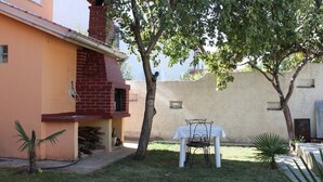A patio area with a table and chairs, a small tree, and a building with a brick chimney. - Apartment 1775/20467 (Istria - Medulin), 750m from the beach (Medulin)