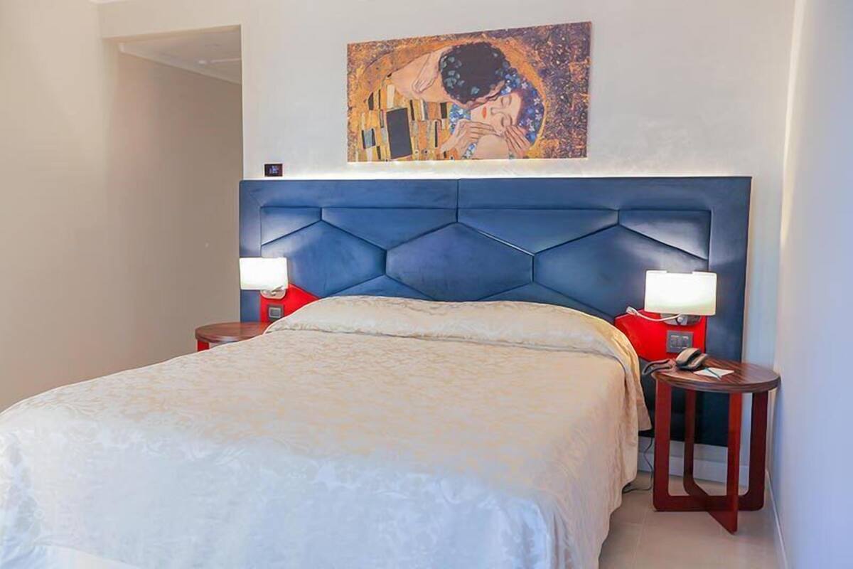 A bedroom with a large bed, two bedside tables, a headboard, and a painting on the wall.