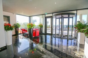 Um saguão com porta giratória, assentos vermelhos e plantas em vasos.