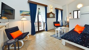 A modern living room with a sofa, armchair, and a small table. There is a TV mounted on the wall, a lamp, and a window with curtains. - Apartment 1787/20945 (Istria - Barbariga), 1500m from the beach (Barbariga)