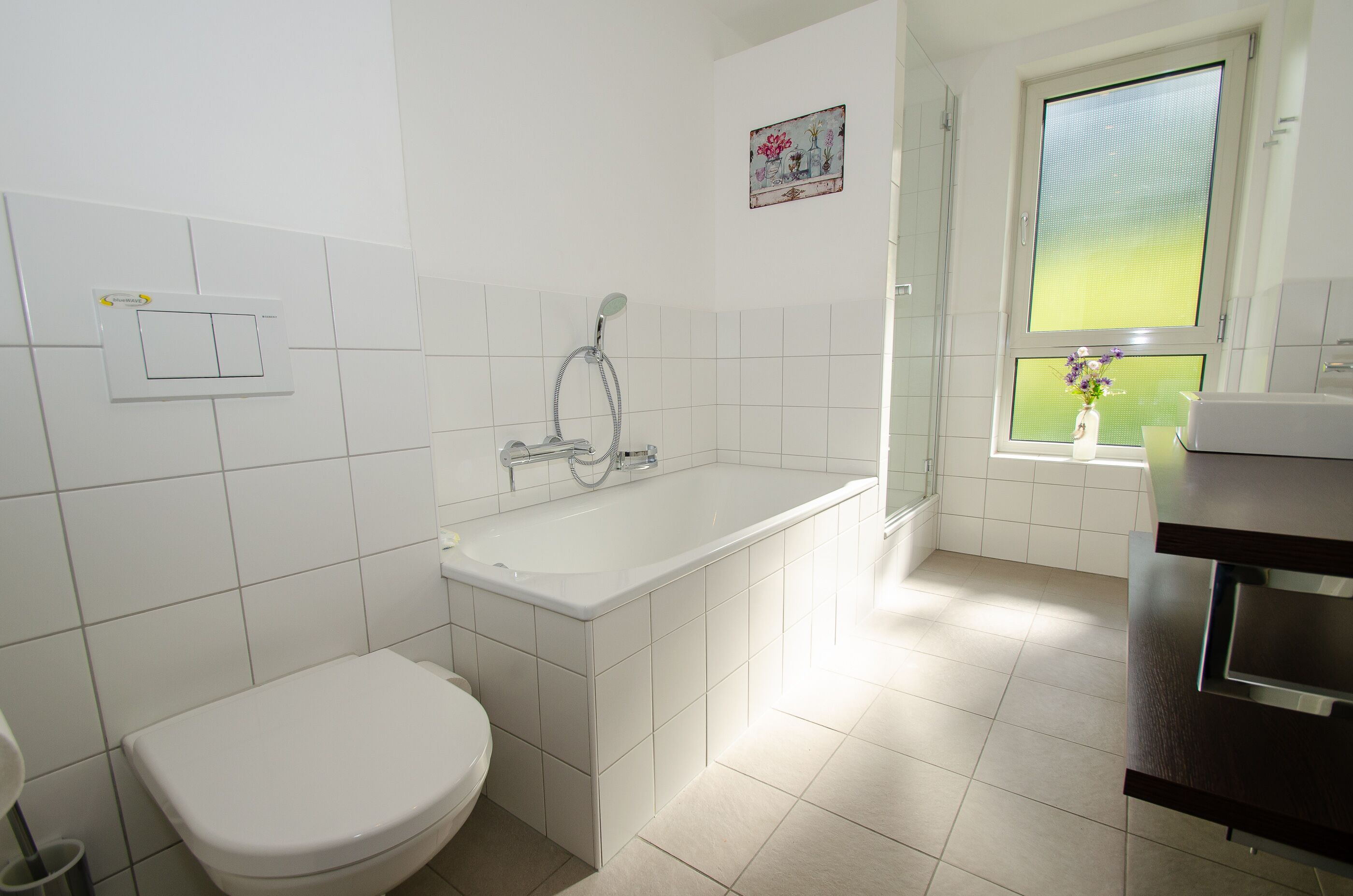 A bathroom with a white toilet, a bathtub, and a window with a view of greenery.