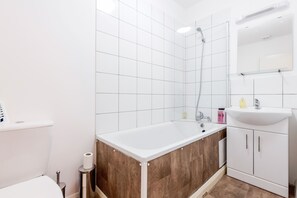 A modern bathroom with a white bathtub, a shower, and a sink. - Manor Lodge Apartments (Watford)