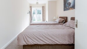 A bedroom with two beds, a window with curtains, a painting on the wall, and a bedside lamp.