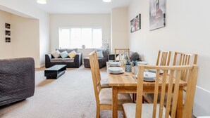 A modern living room with a sofa, a dining table with chairs, and a large window.