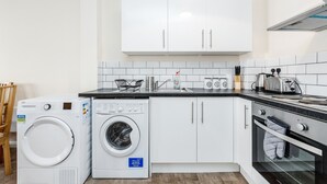 A compact kitchen with white cabinets, a washing machine, a toaster, and an oven.