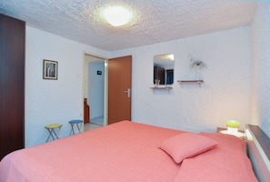 A bedroom with a bed, a mirror, a small plant, and a nightstand.