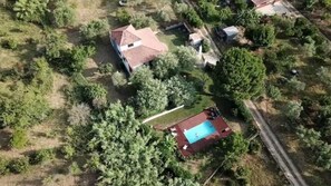 An aerial view of a residential area with a swimming pool, multiple houses, and surrounding greenery.
