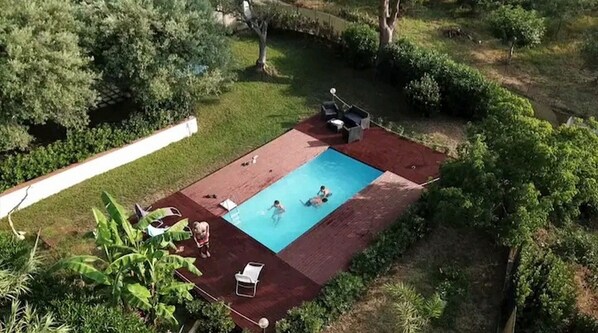 Un jardin avec une piscine, entouré de verdure et doté d’une terrasse rouge.