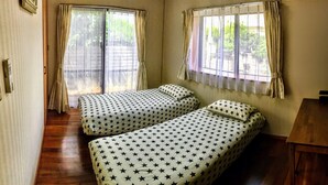 A room with two single beds, a wooden floor, a small table, and a window with curtains. - White House (Onna)