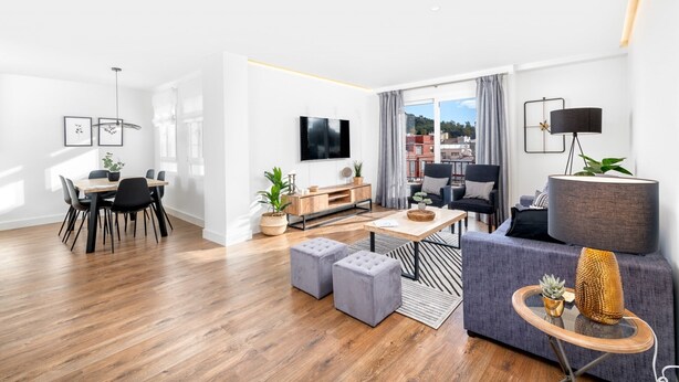 Una sala de estar moderna con piso de madera, un sofá gris, un televisor y un comedor con mesa y sillas.