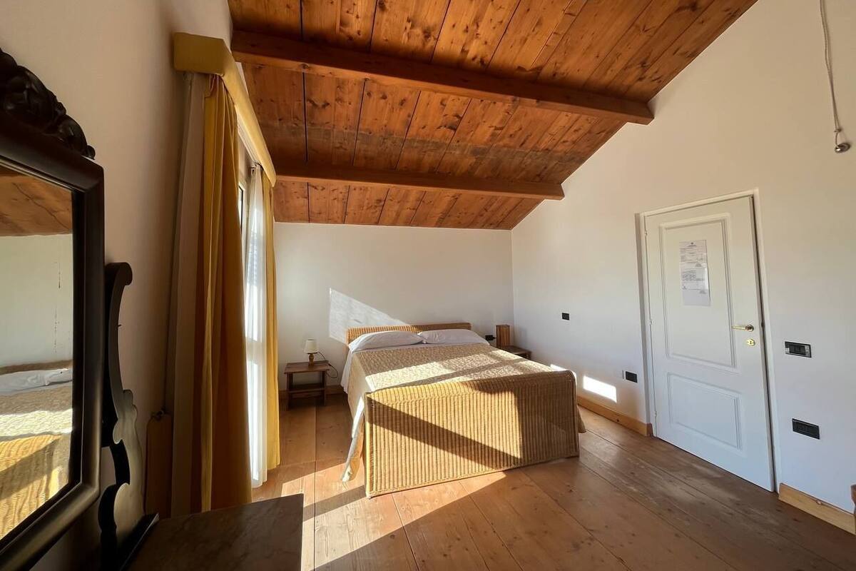 Une chambre à coucher avec un plafond en bois, un lit, une table de chevet, une porte et une fenêtre avec des rideaux.