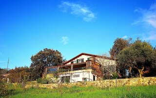 Una casa rústica con pared de piedra, un balcón y un jardín delantero.