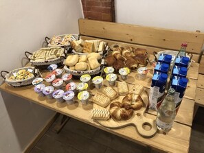 A wooden table with various food items and drinks, including bread, pastries, and bottled water. - Hotel Alla Prisa (Carisolo)